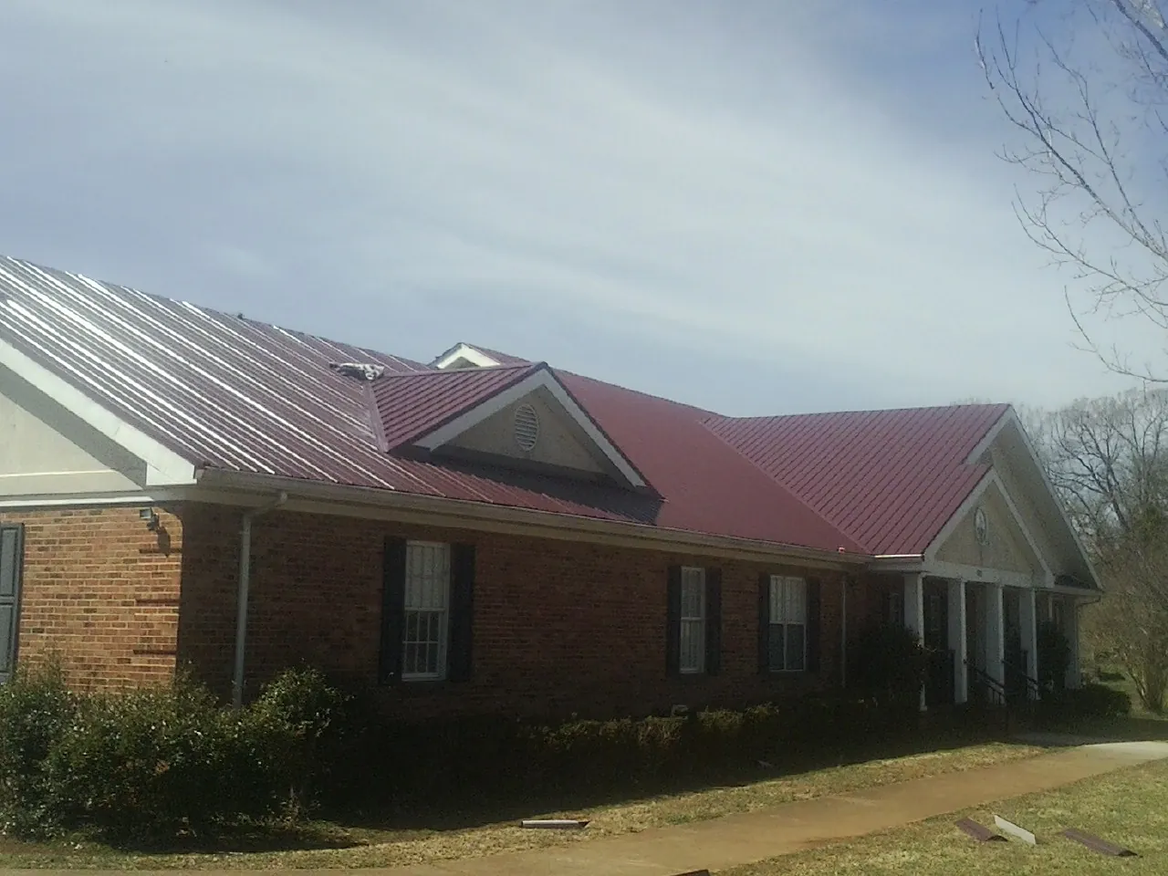 Red metal roof with gabled entries on a long brick building, from a Hail Damage Roof Repair job in Meredith
