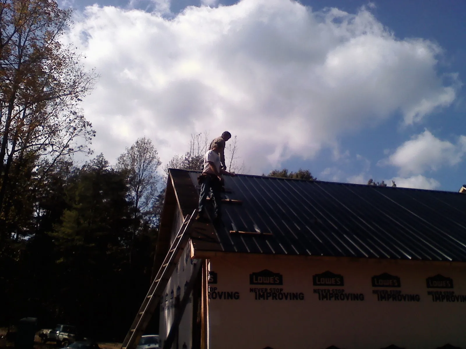 Roofer fastening dark metal panels high against a cloudy sky, from a Roof Inspection job in Meredith