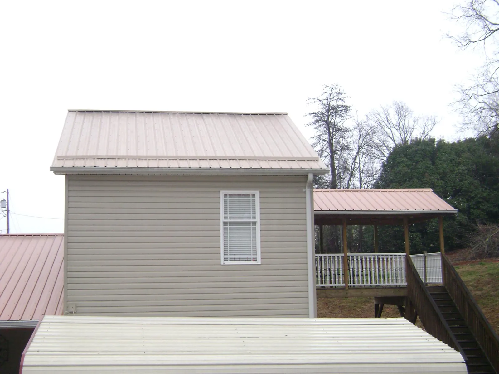 Tan metal roofs on a two story addition and attached porch, from a Roof Replacement job in Meredith